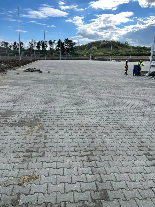 Nagy ipari parkoló kész térkő burkolata kandeláberekkel, szegélyezés közben